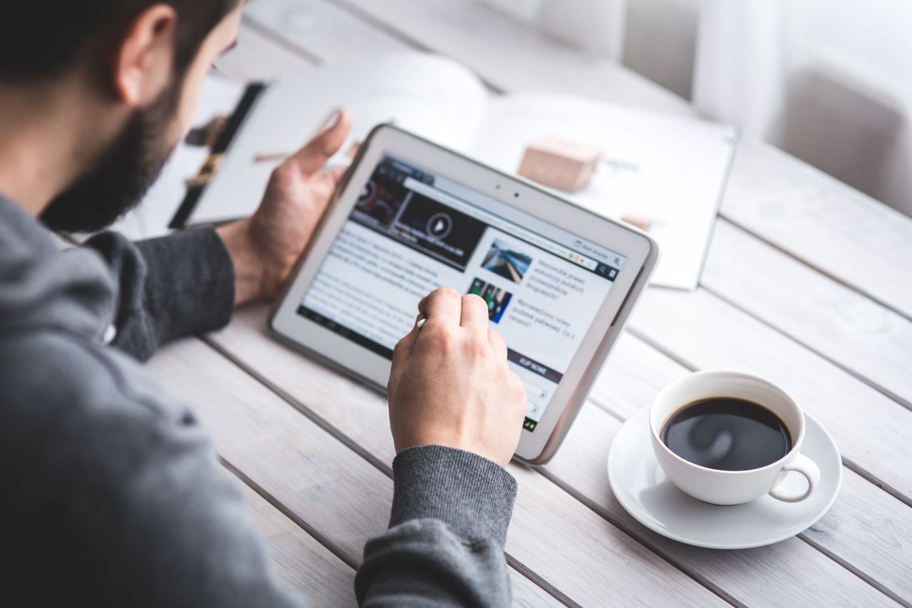 why-choose-us A man uses a tablet to browse news while enjoying a cup of coffee, stylus in hand.