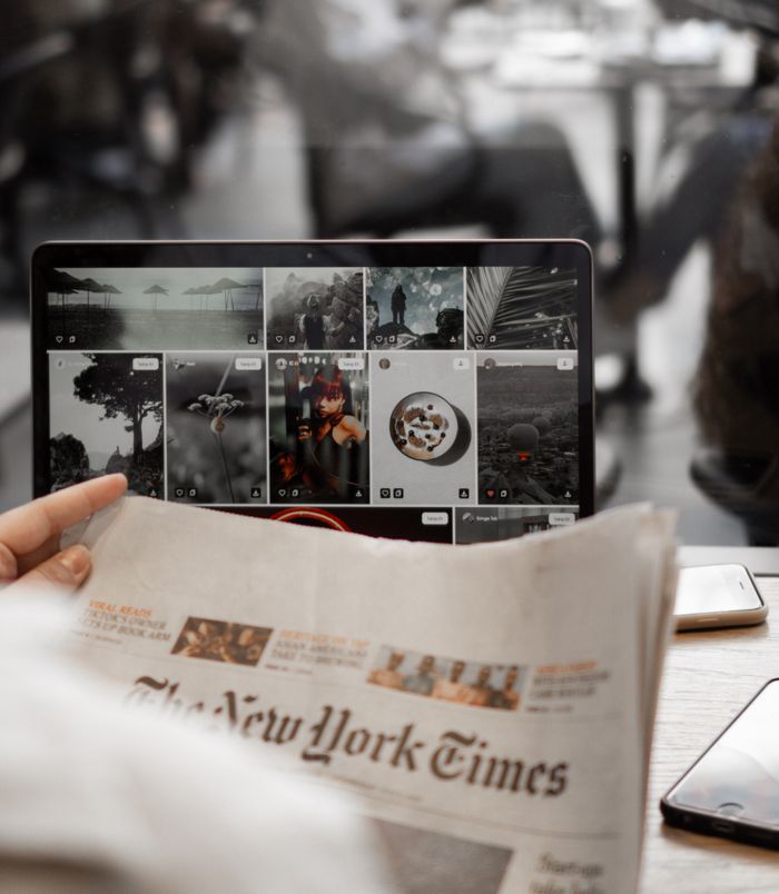 creative-02 A person reading a newspaper while browsing images on a laptop, symbolizing remote work lifestyle.
