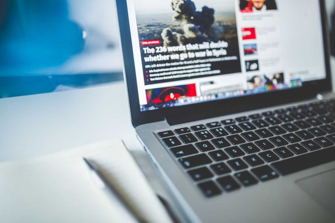 digital Open laptop displaying an online news article on a desk with a notebook nearby.