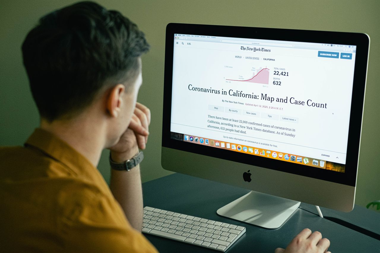 creative A man reading a coronavirus case count article on a computer screen indoors.